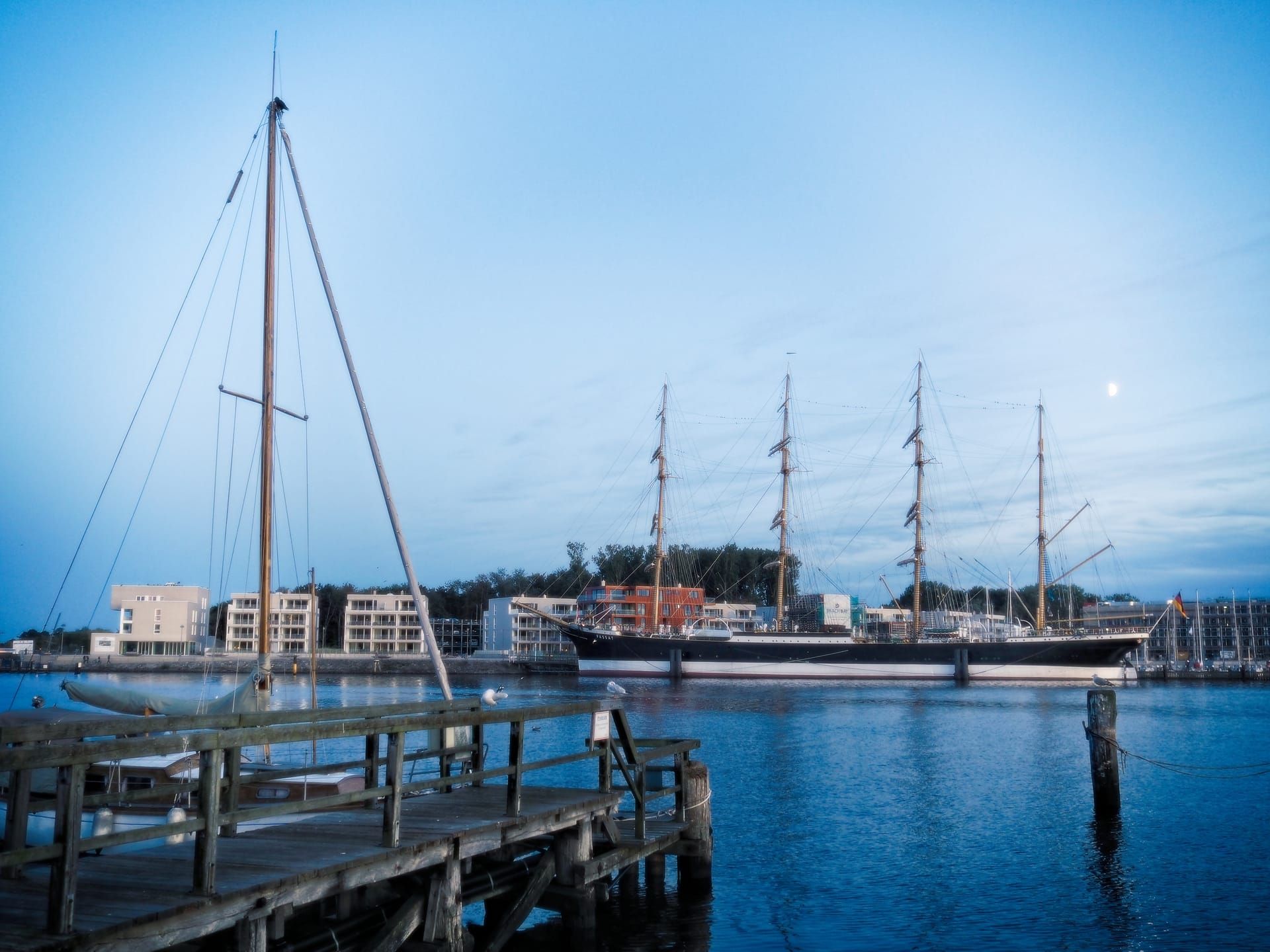 Die Viermastbark Passat am Priwall in der blauen Stunde, vorn ein hölzerner Steg und der Mast eines Segelboots