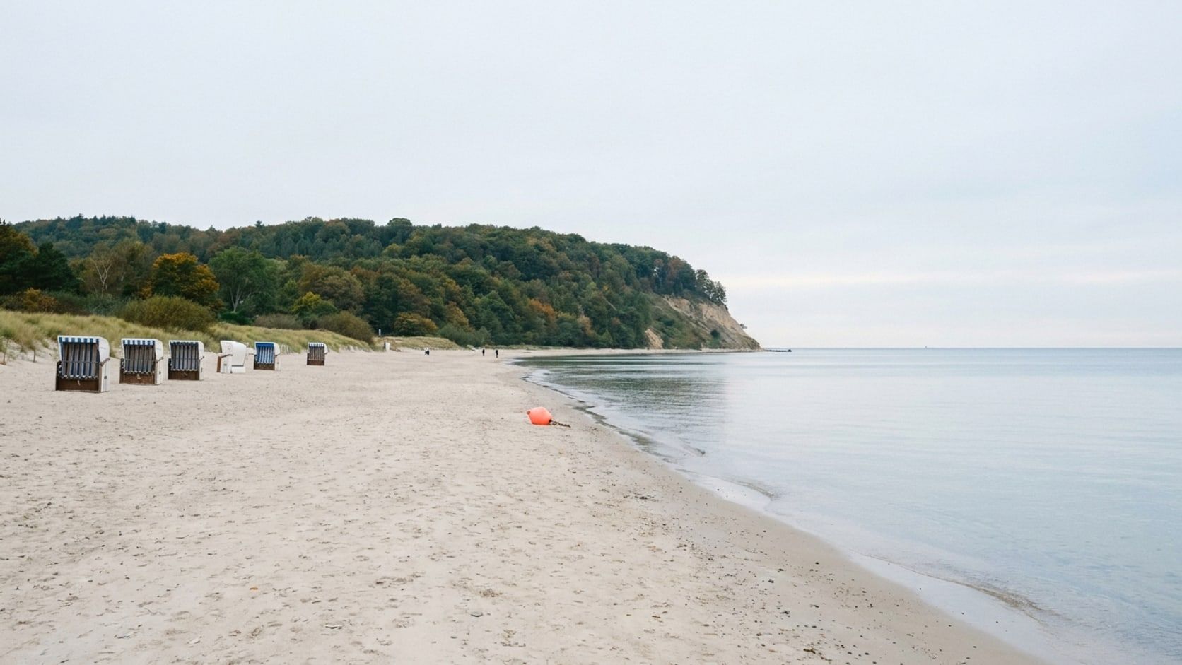 Einige letzte, geschlossene Strandkörbe am fast leeren Strand, dahinter der bewaldete Hang der Hermannshöhe, stille Ostsee
